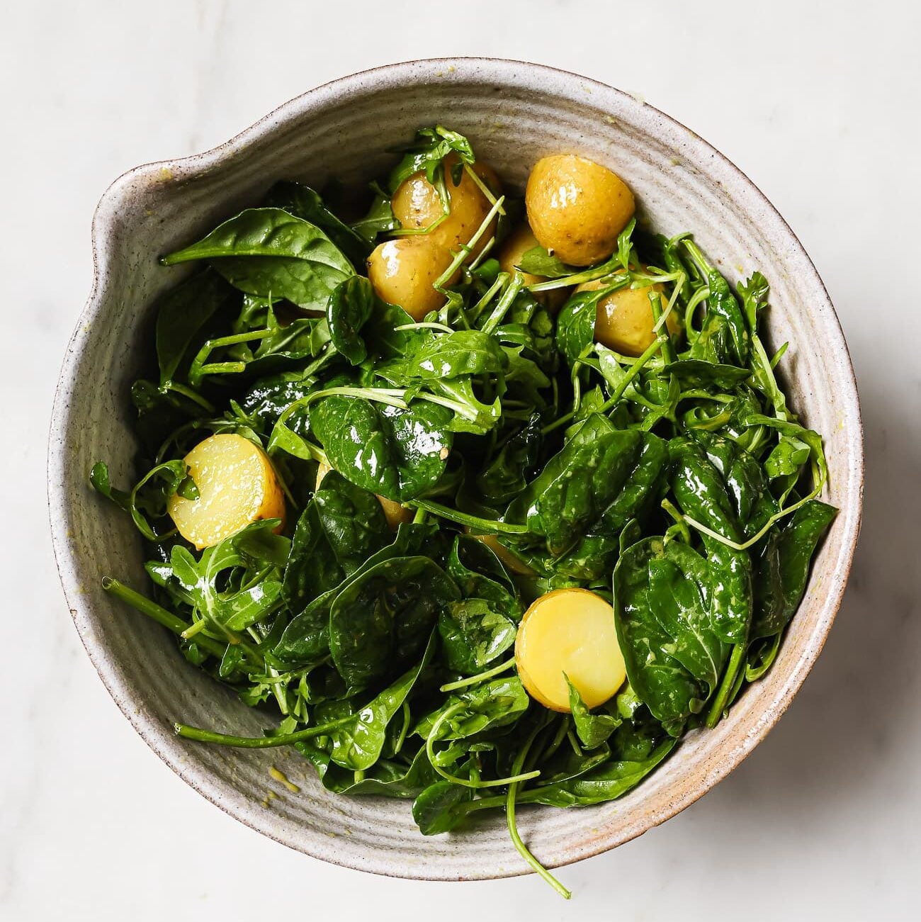 Baby potatoes are added to the bowl of mixed greens.