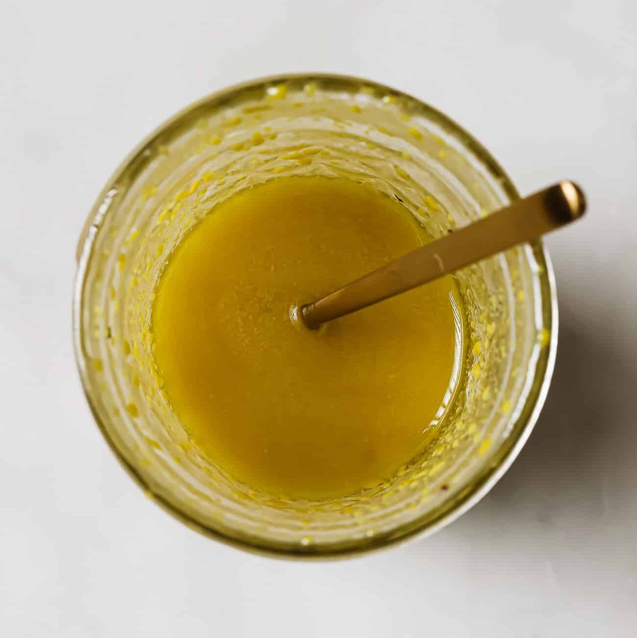 A mason jar of salad dressing with a gold spoon in it.