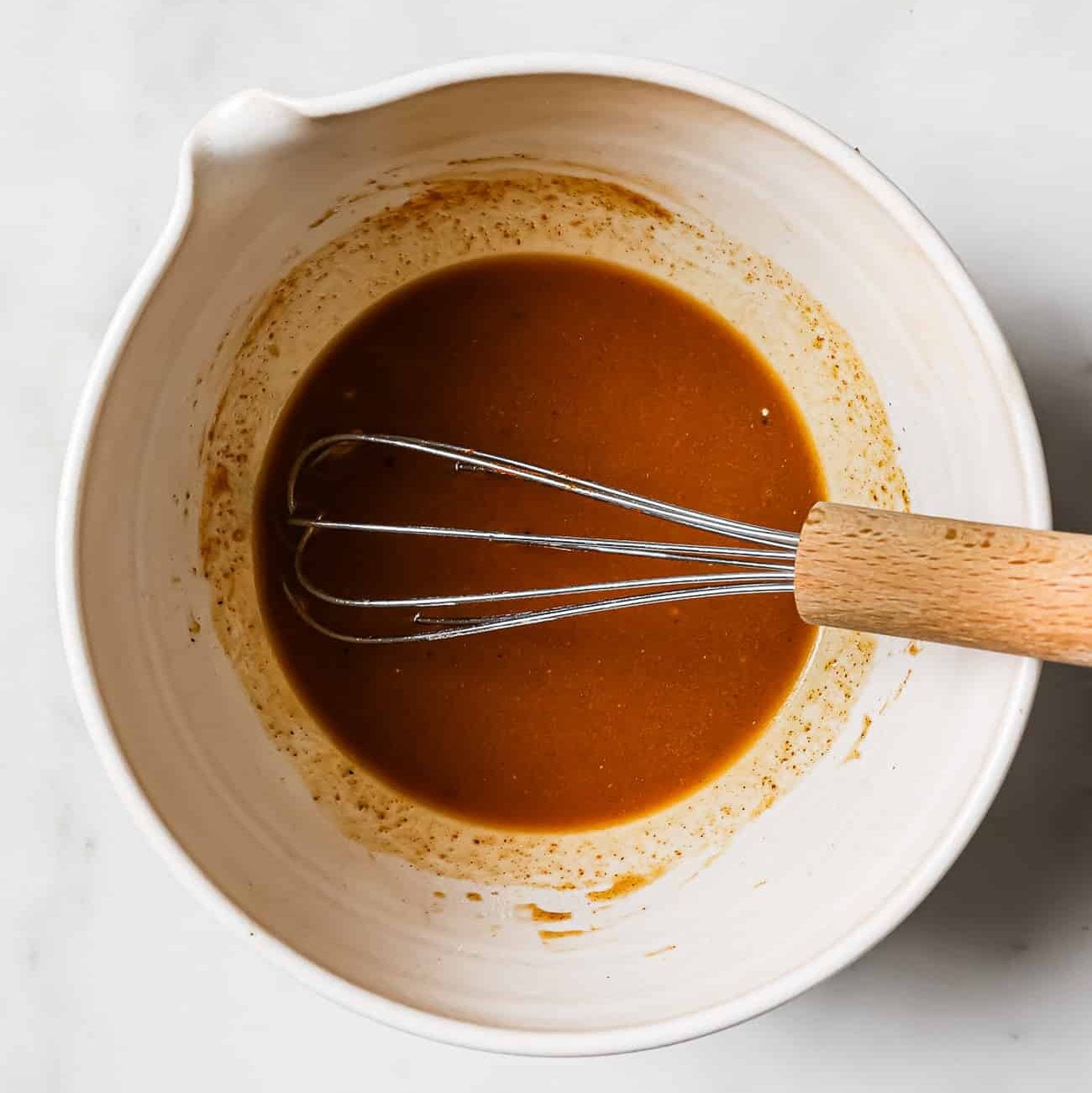 Chicken taco marinade in a white bowl with a whisk in it.