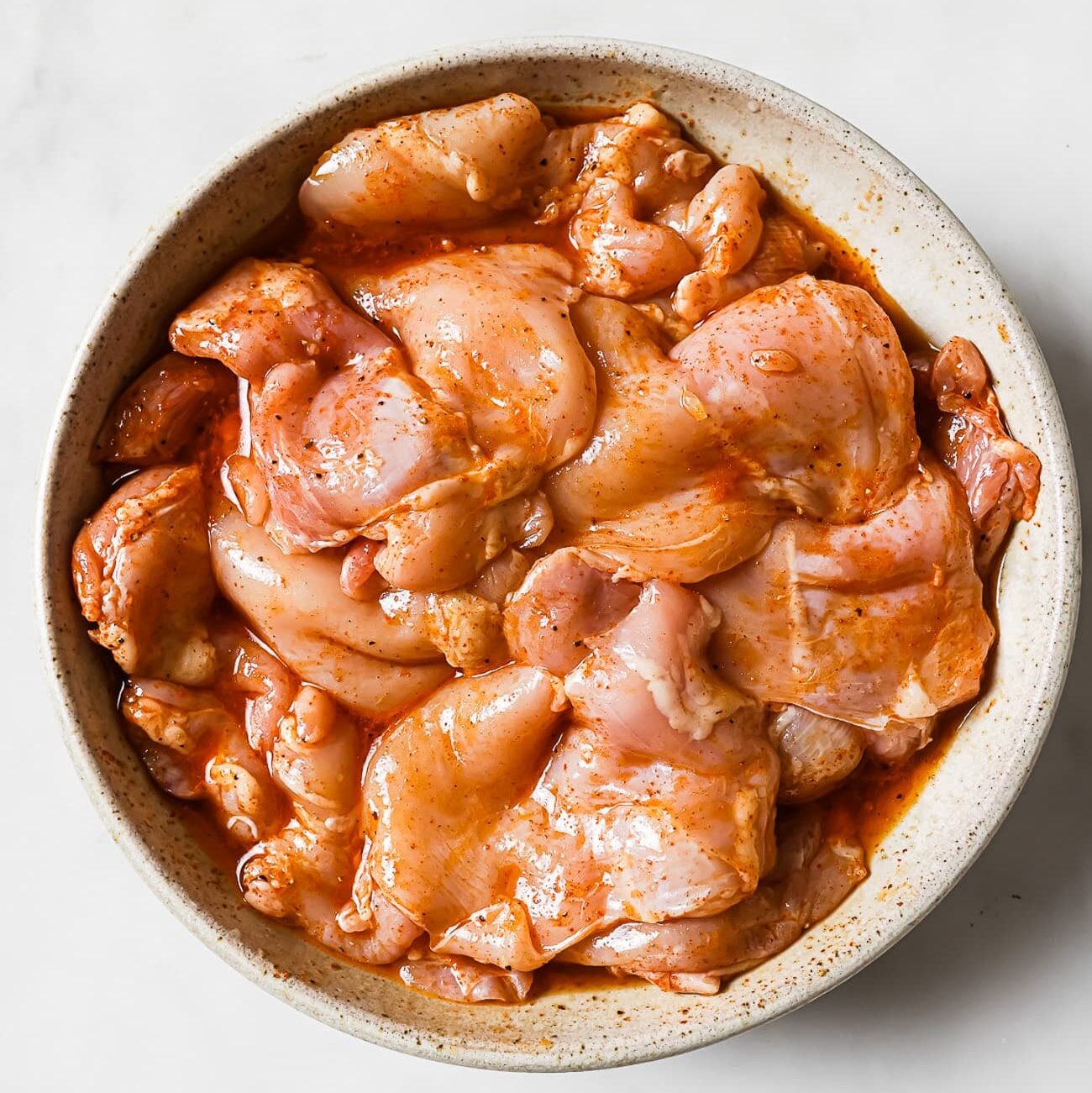 Chicken thighs coated with marinated in a large white bowl.