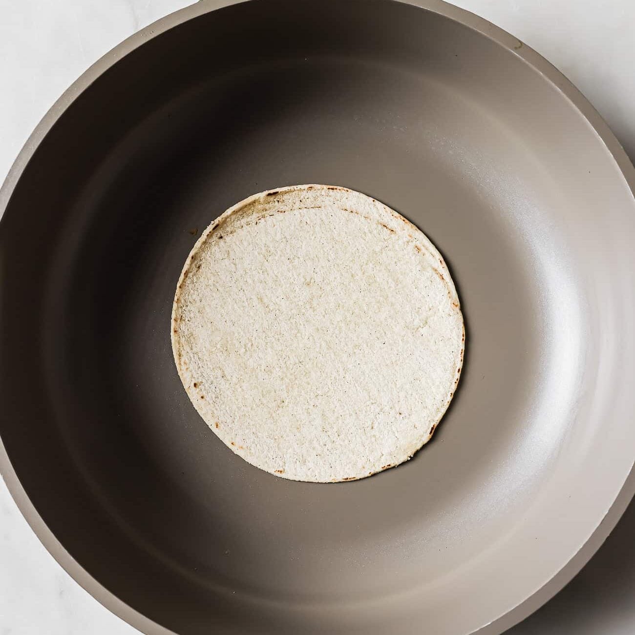 A corn tortilla in the middle of a large skillet.
