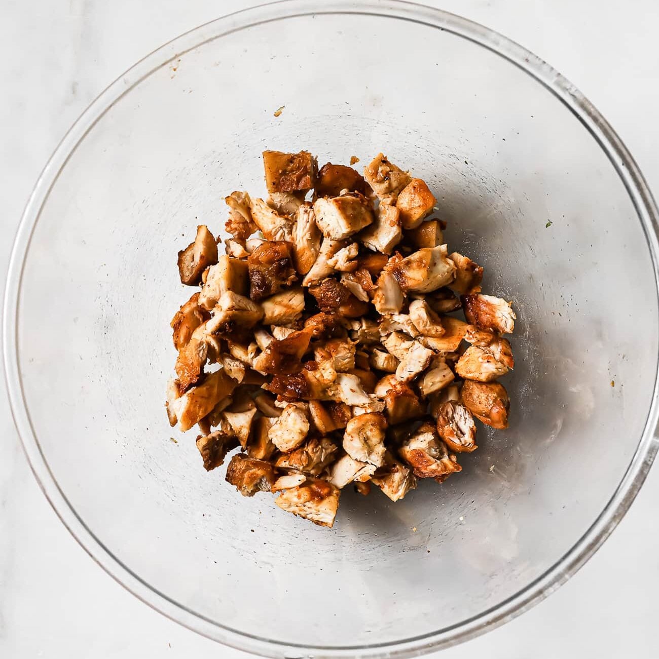 Diced chicken thighs in a clear bowl on a white countertop.