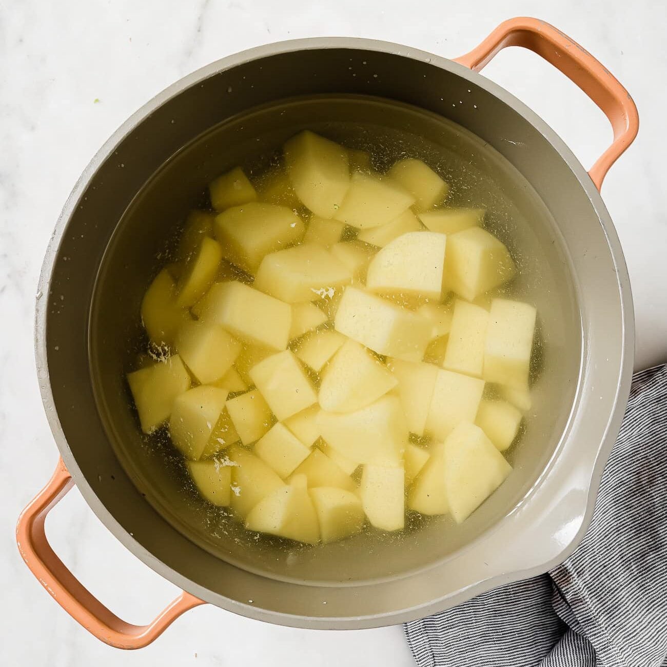 Diced potatoes in a large pot of water on a white countertop.