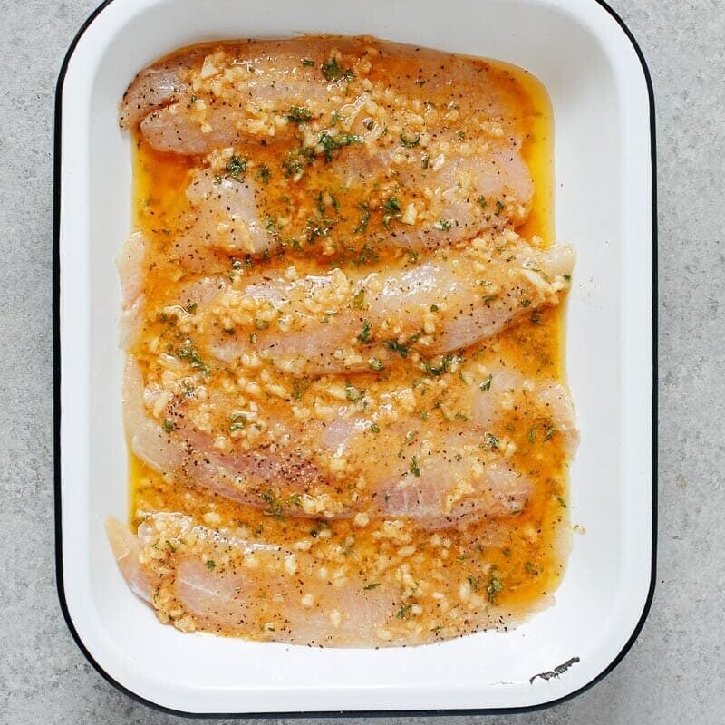 raw tilapia inside of a white baking sheet with garlic butter sauce