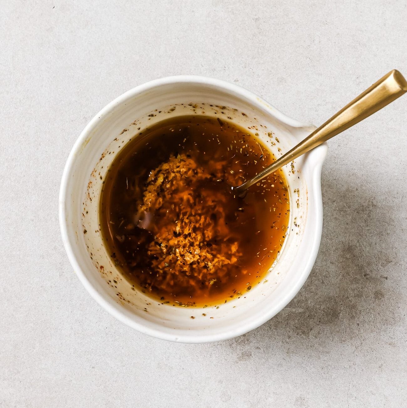 Greek chicken marinade in a white mixing bowl with a gold spoon in it.