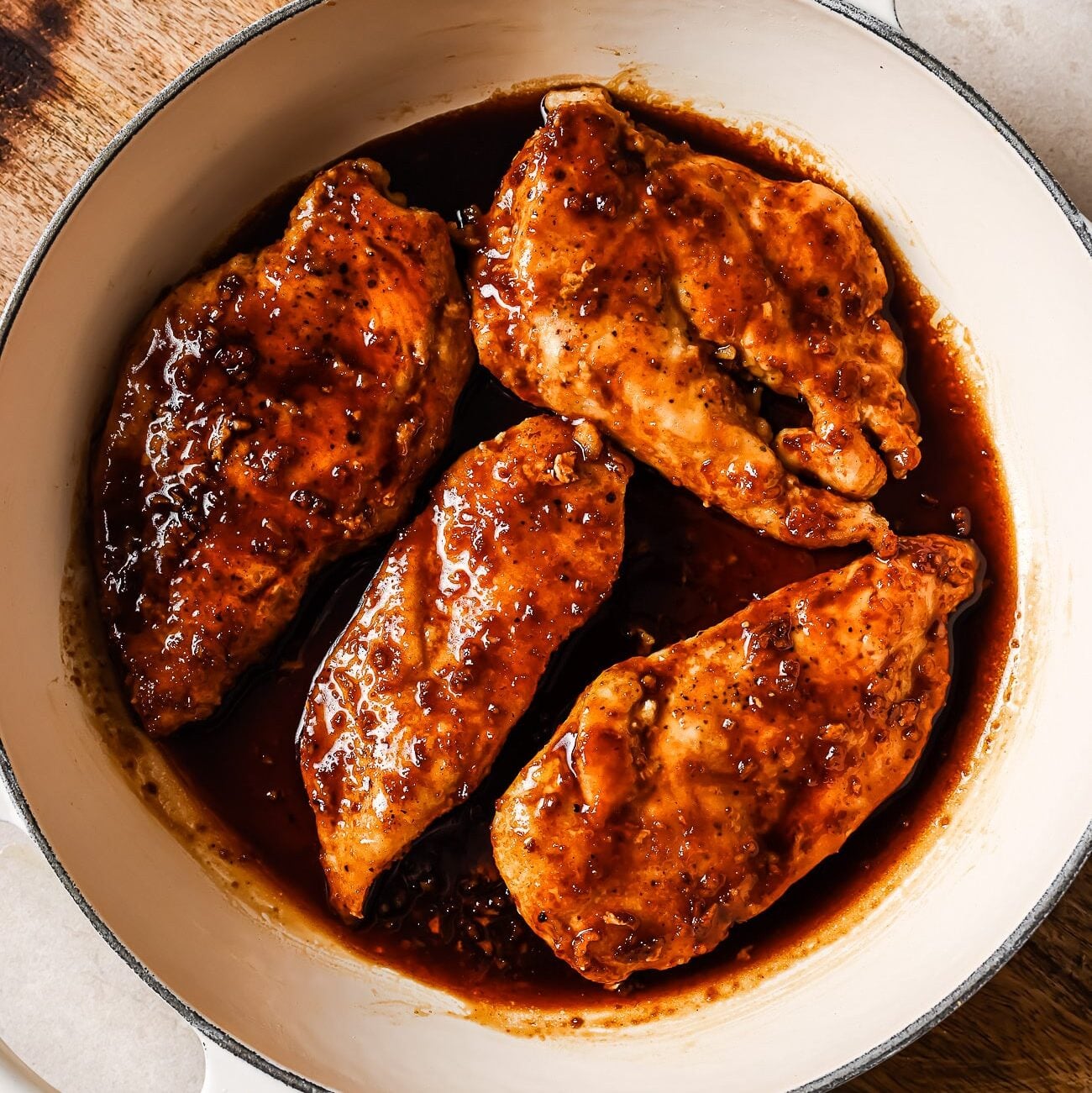 Honey garlic chicken breasts covered in sauce in a white skillet.
