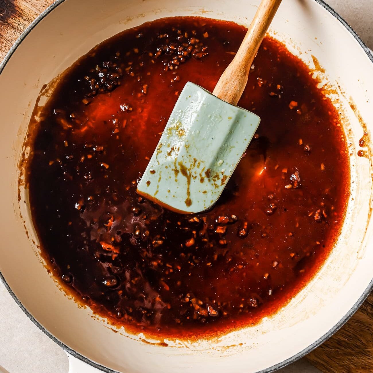 Sticky honey garlic sauce in a white skillet with a blue rubber spatula in it.