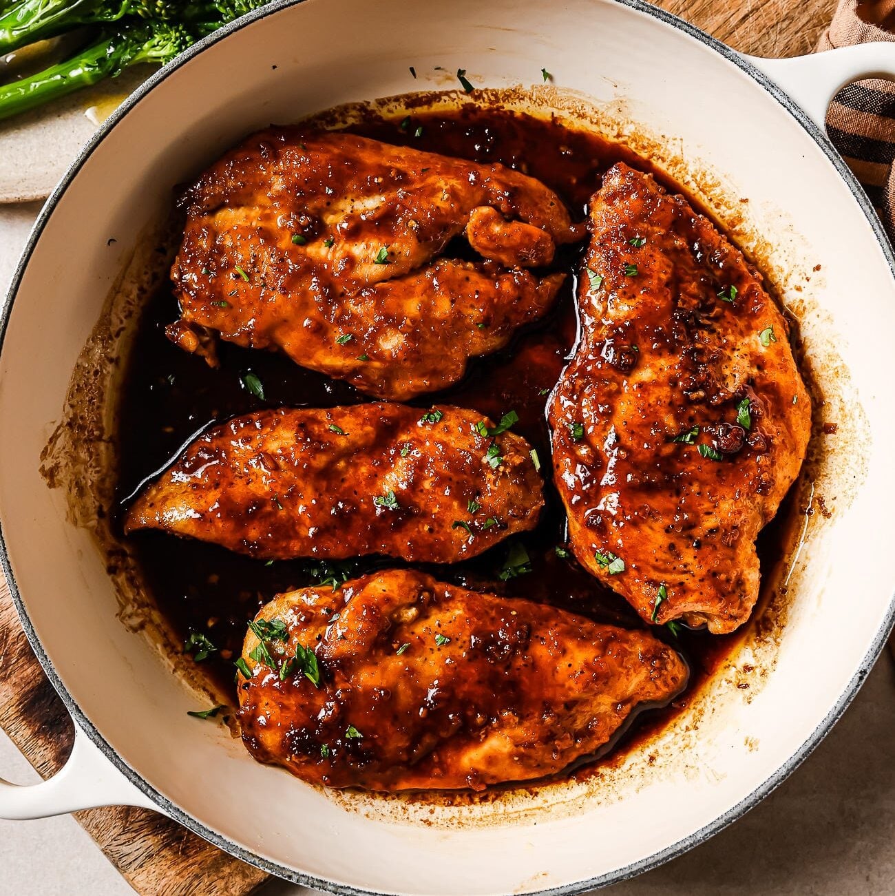 Honey garlic chicken breast garnished with fresh parsley in a white skillet with broccoli on the side.