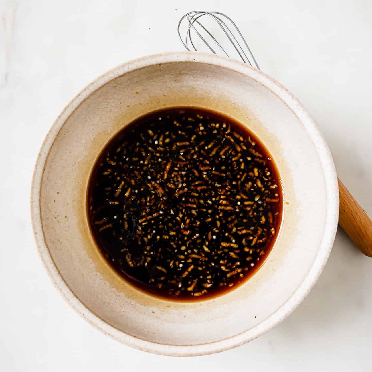 A small bowl of sauce with a whisk on the side.