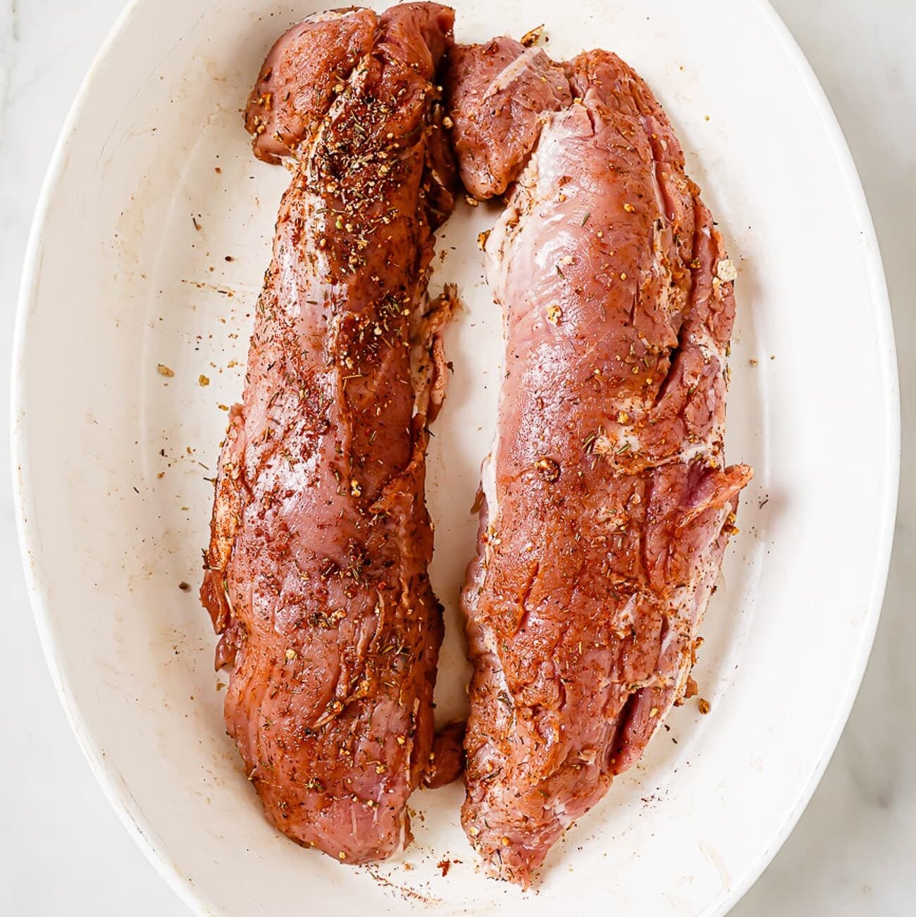 Two seasoned pork tenderloins in a baking dish.