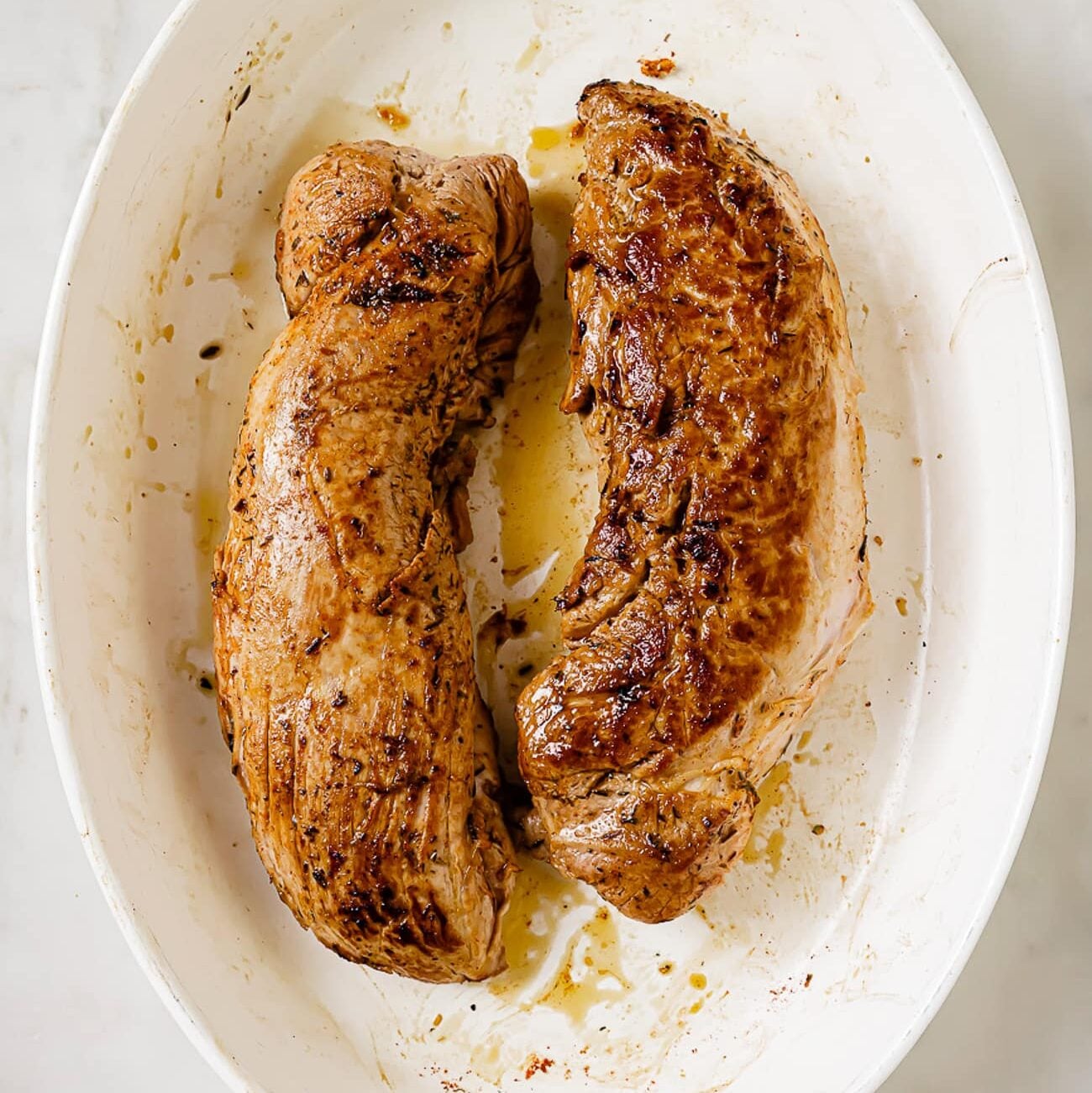 Two seared pork tenderloins in a baking dish.