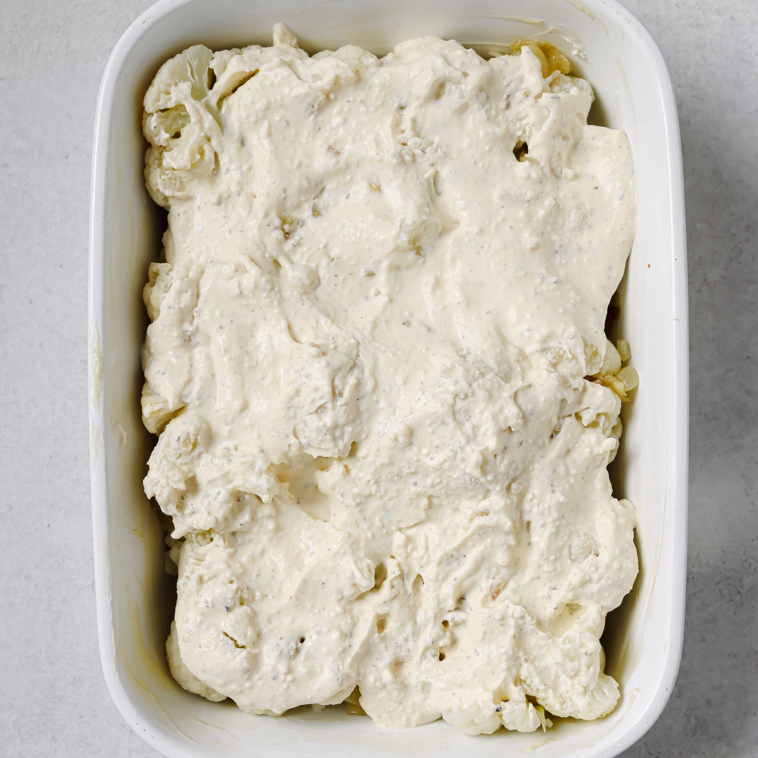Cauliflower with cream cheese sauce in a white casserole dish.