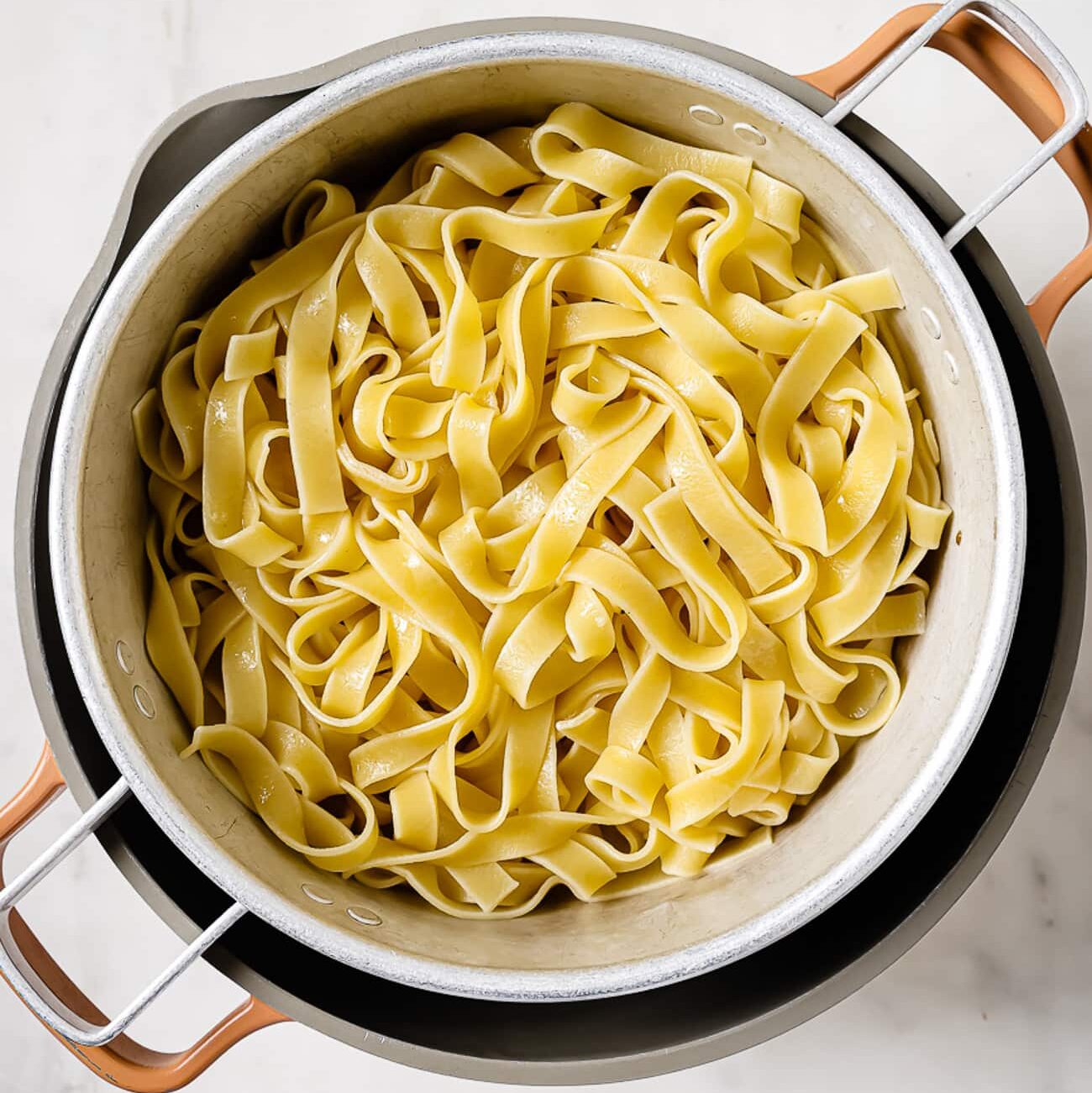 An overhead view of cooked and drained fettuccini noodles in a colander.