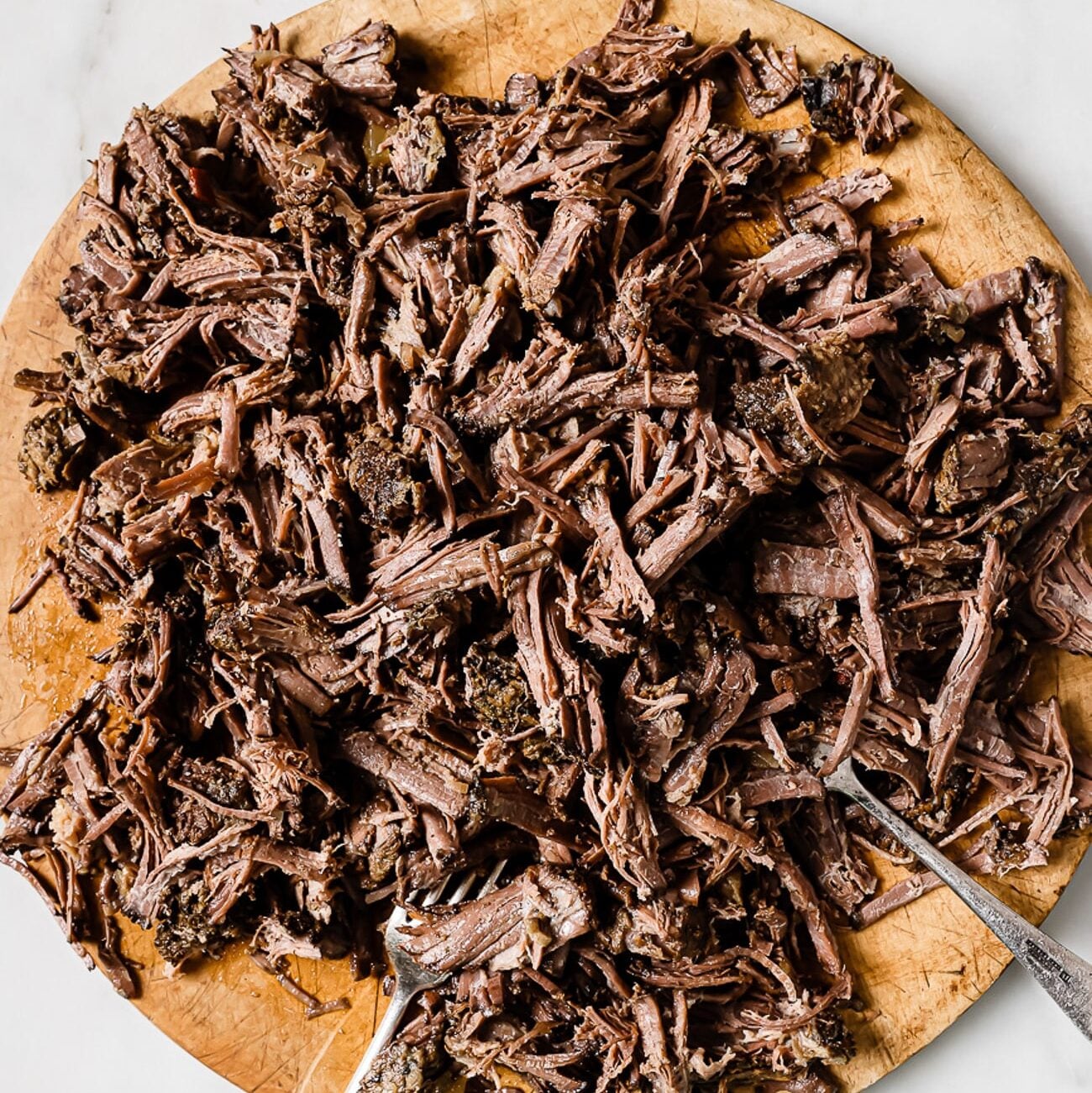 Shredded barbacoa on a wooden cutting board.