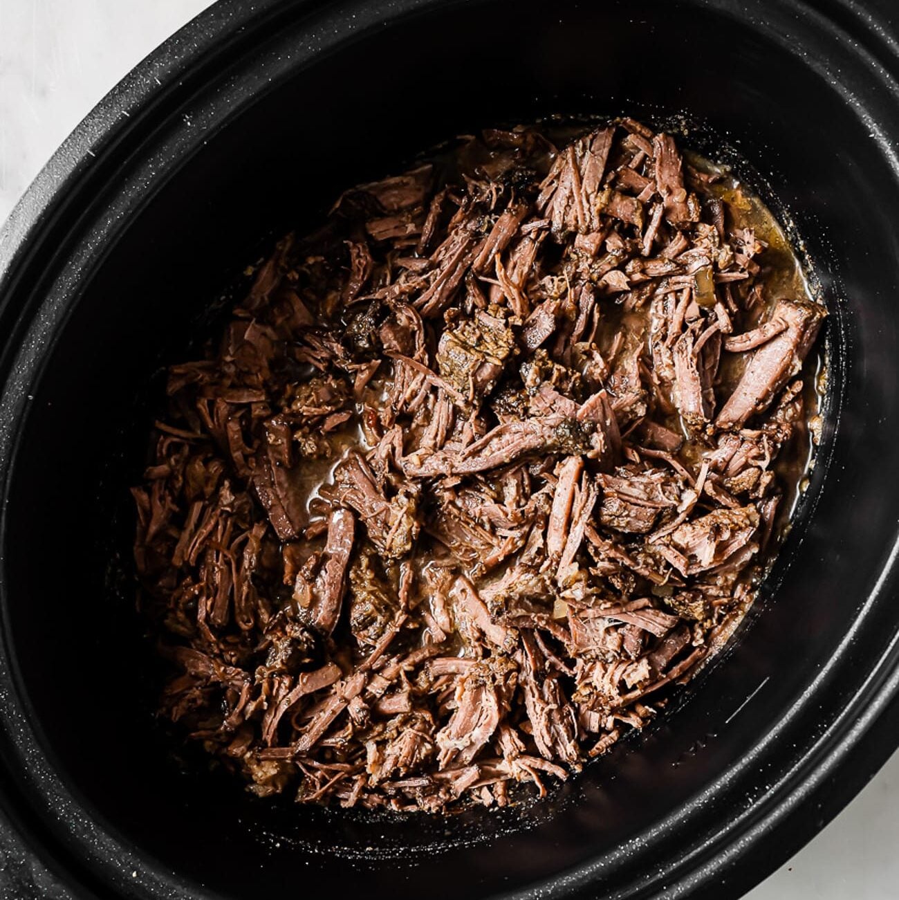 The shredded barbacoa is placed back in the crockpot.