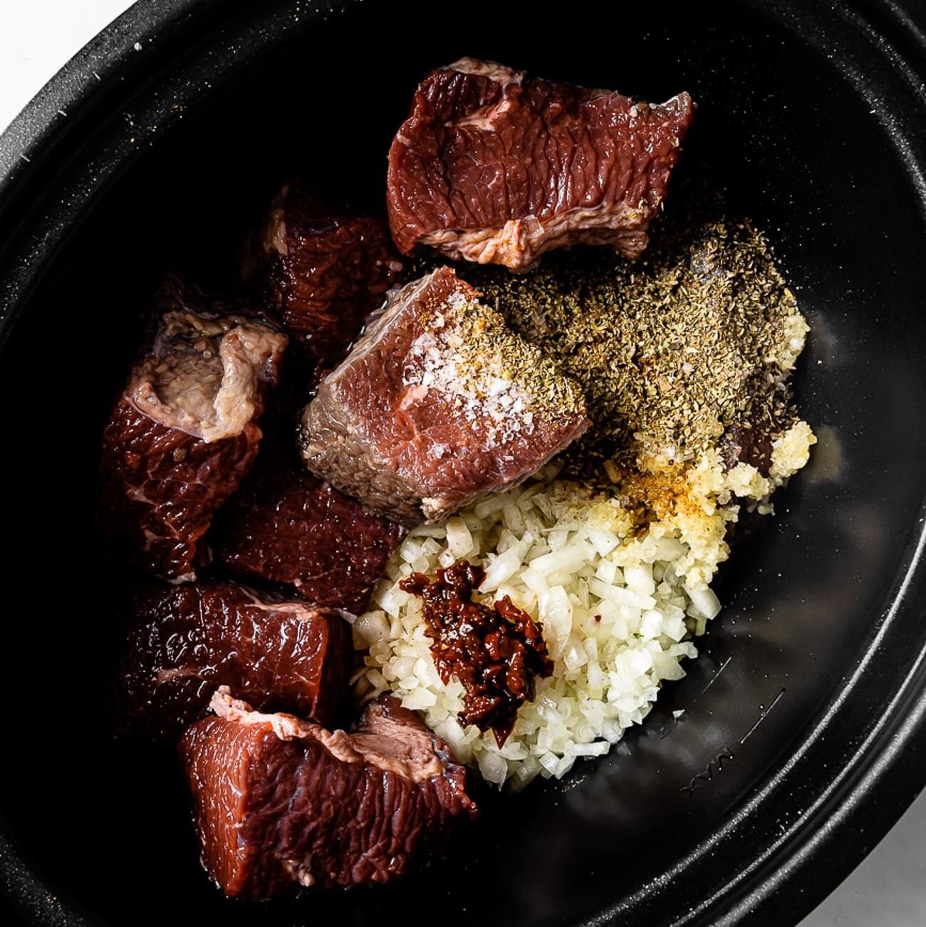 Beef, onions, garlic, and seasonings in a slow cooker.