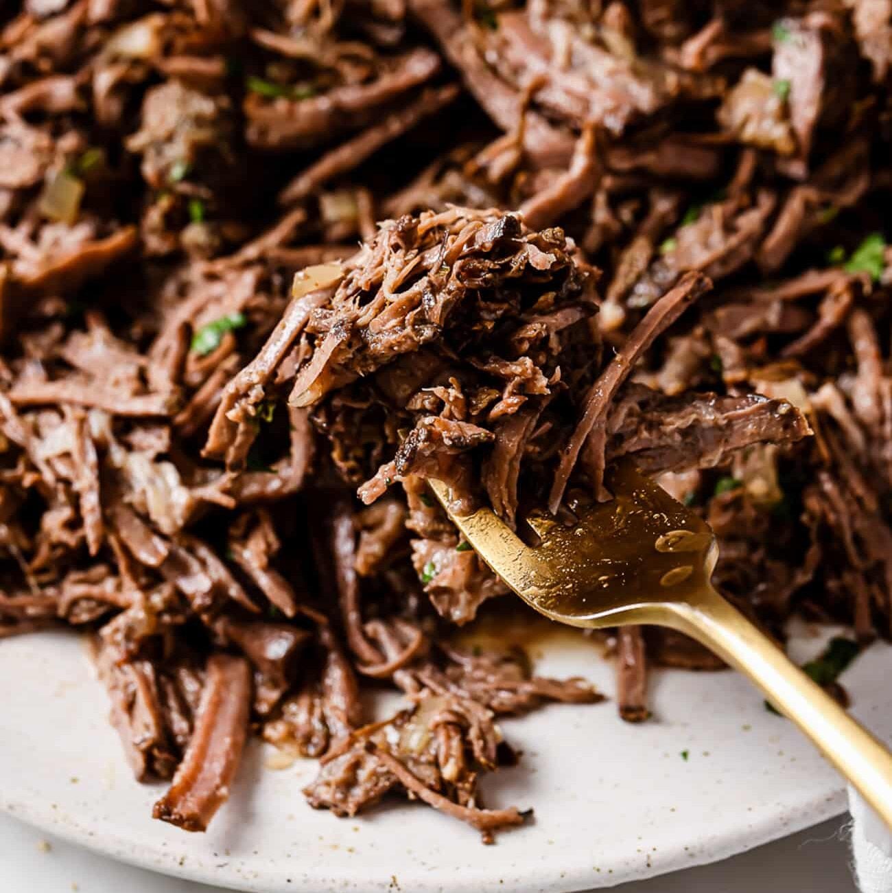 Shredded barbacoa on a white plate with a gold fork on the side.