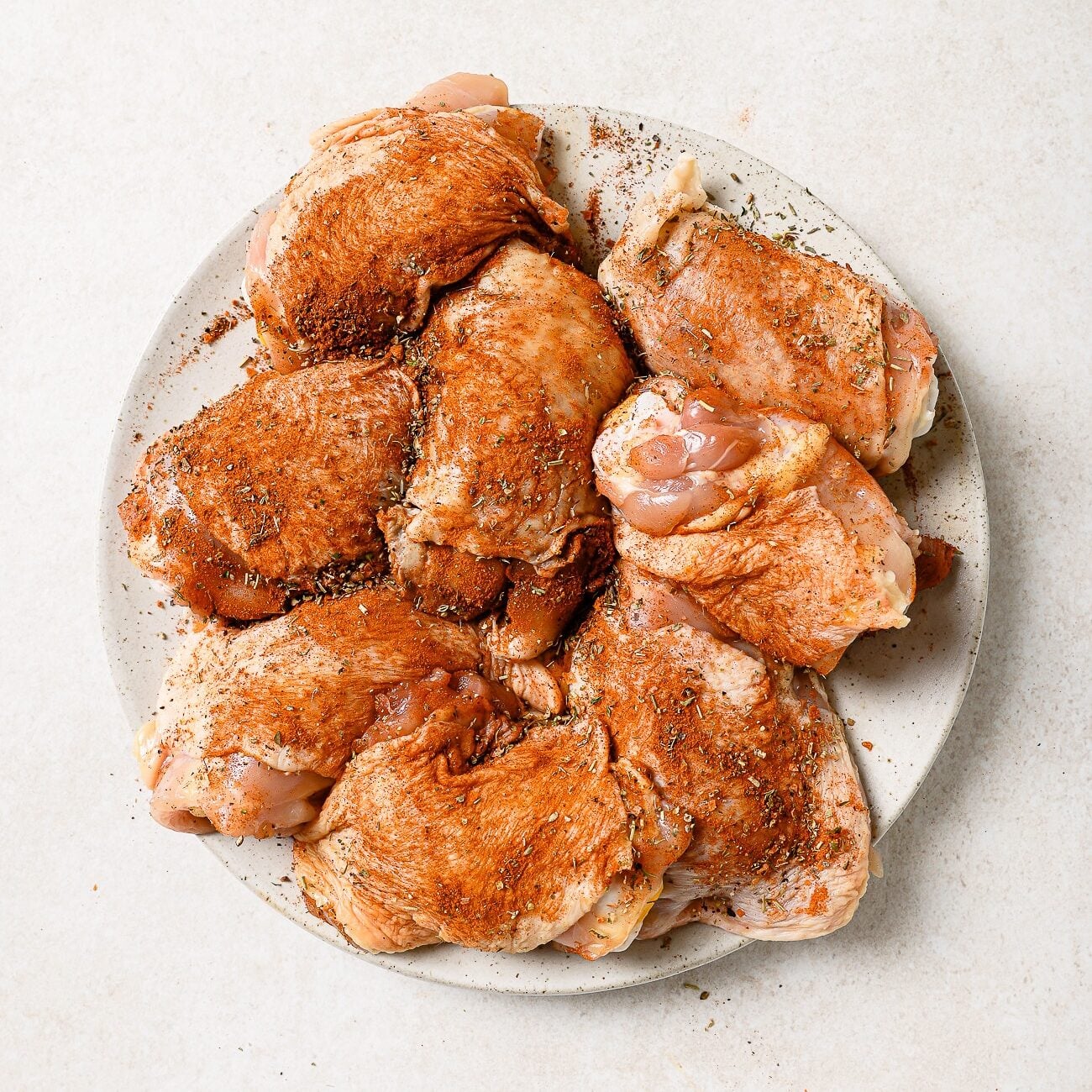 An overhead view of seasoned chicken thighs arranged on a white plate.