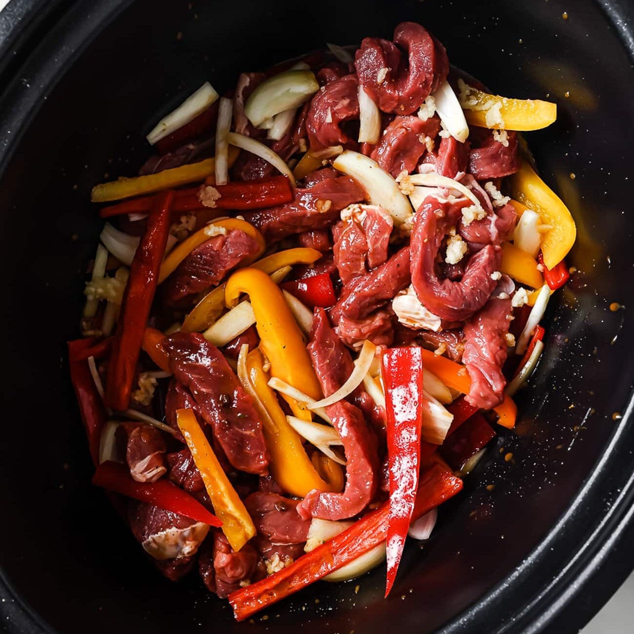 Bell peppers, onions, garlic, and sliced steak in the slow cooker.