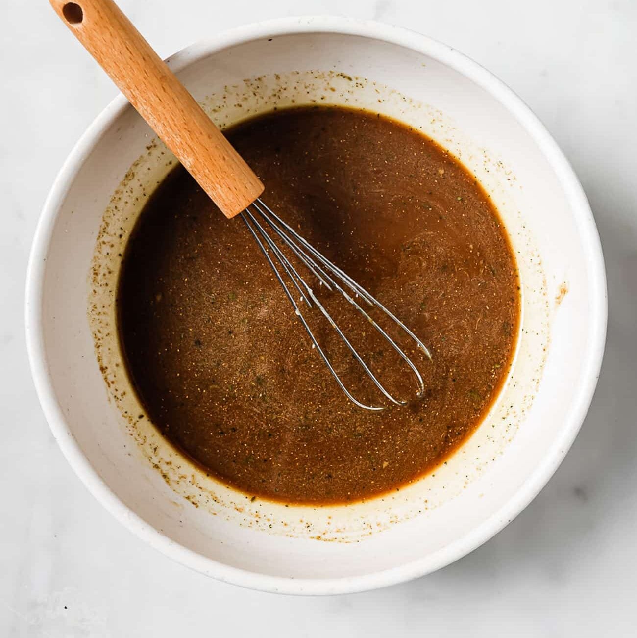 A small bowl of pepper steak sauce with a whisk in it.