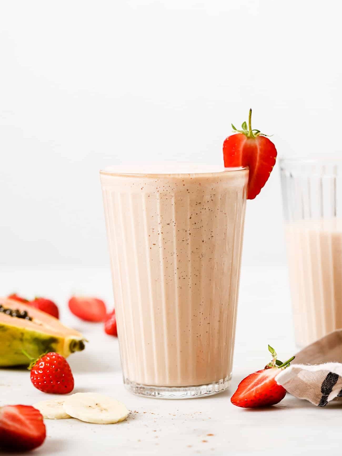 A papaya smoothie in a tall glass garnished with a strawberry slice.