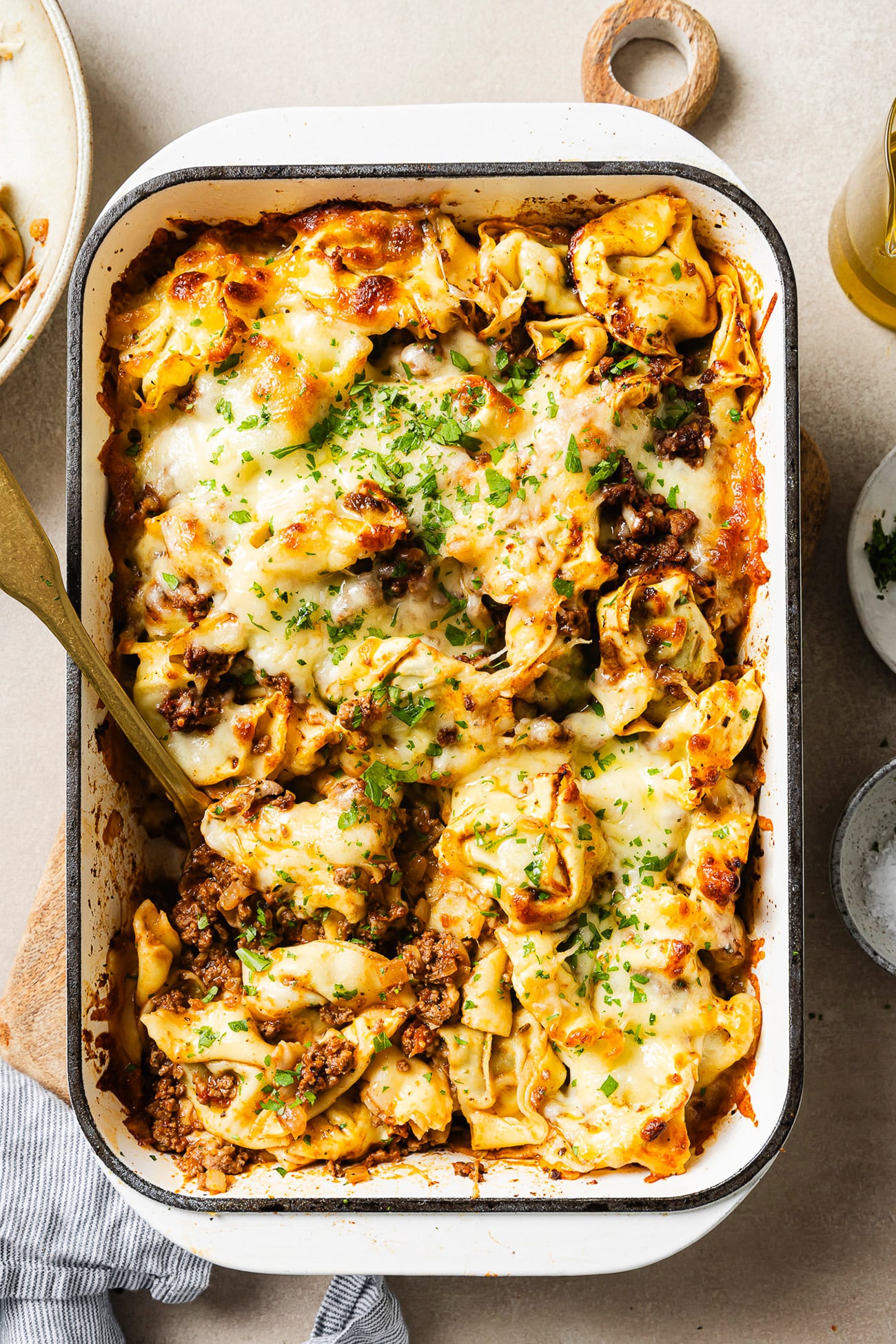 baked tortellini with ground beef in a white 9x13 baking dish, golden melted mozzarella on top, garnished with fresh parsley