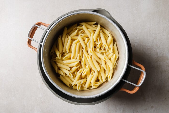 A pot filled with cooked penne pasta, viewed from above, sitting on a light-colored surface.