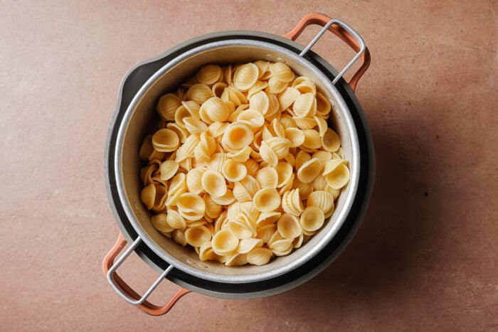 A pot filled with cooked orecchiette pasta sits on a brown countertop, viewed from above.