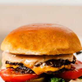 A juicy Smash Burger Recipe with melted cheese, lettuce, tomato, and sauce in a shiny brioche bun sits on parchment paper. Text above reads The Easiest Smash Burgers. Logo at bottom says Primavera Kitchen.