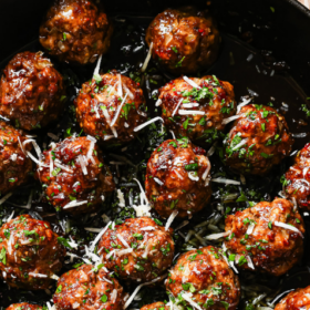 A skillet filled with savory Honey Garlic Meatballs, topped with chopped herbs and shredded cheese, photographed from above. Text reads Honey Garlic Meatballs.