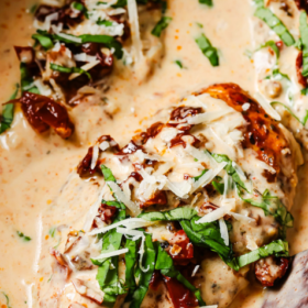 Crock Pot Marry Me Chicken breasts in a creamy sauce with sun-dried tomatoes, topped with shredded cheese and fresh basil.