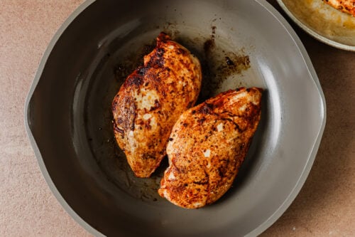 Two seared chicken breasts cooking in a grey skillet.
