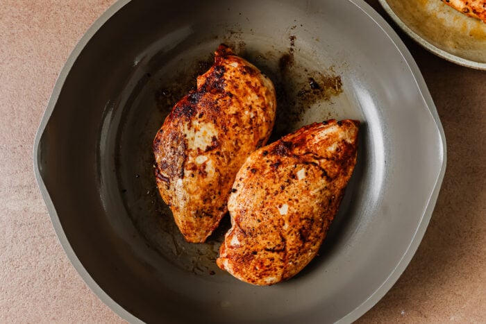 Two seared chicken breasts cooking in a grey skillet.