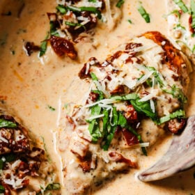 Chicken breasts in a creamy sauce topped with sun-dried tomatoes, shredded cheese, and fresh basil.