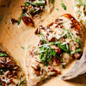 Chicken breasts in a creamy sauce topped with sun-dried tomatoes, shredded cheese, and fresh basil.