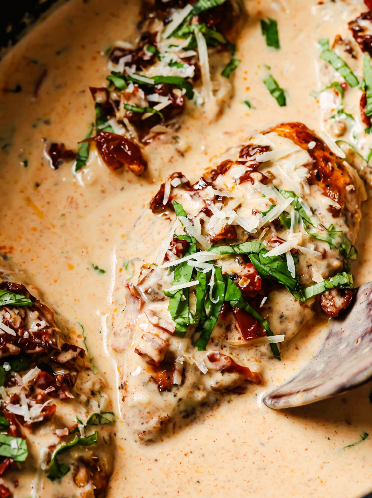 Chicken breasts in a creamy sauce topped with sun-dried tomatoes, shredded cheese, and fresh basil.