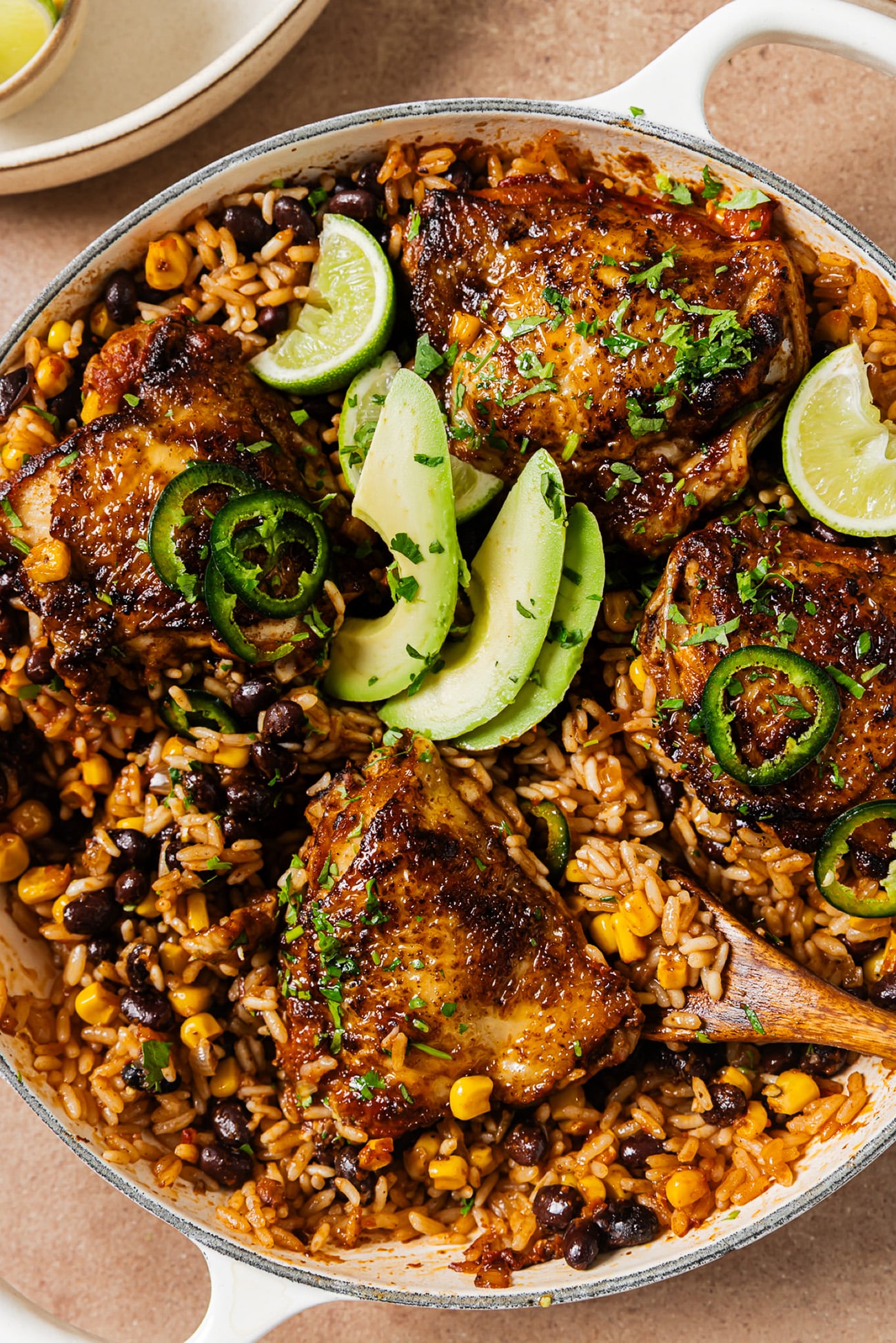 Mexican chicken and rice in a white skillet with crispy chicken thighs, black beans, corn, avocado, and lime.