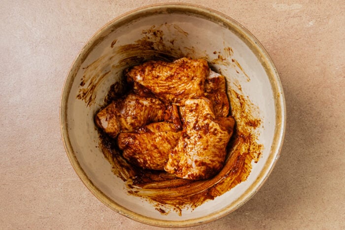 Raw chicken pieces coated in a dark reddish-brown marinade inside a ceramic bowl.