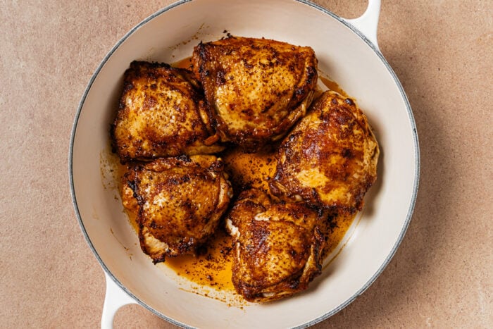 Five seasoned, pan-seared chicken thighs in a white enameled skillet.
